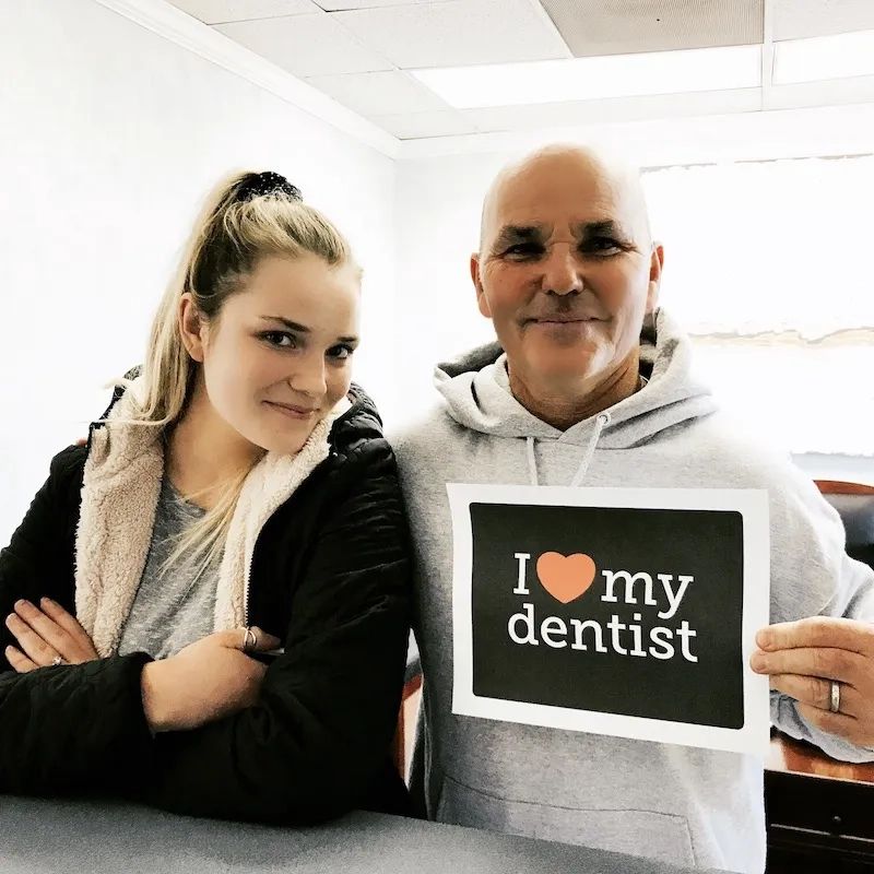 A patient holding an 'I love my dentist' sign next to Dr. Frickman
